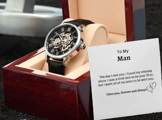 A black watch inside a lined box with a printed message on a card